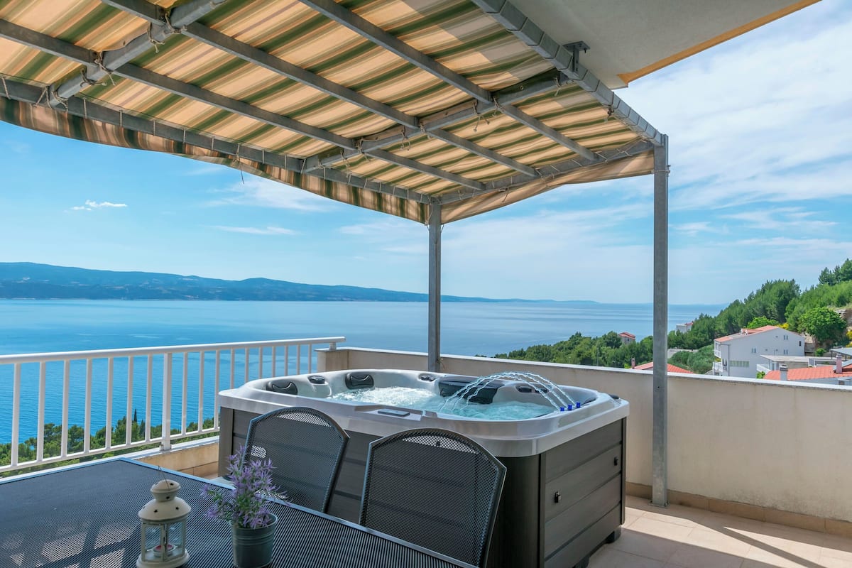 A balcony with a hot tub, a table with chairs, and a view of the sea.