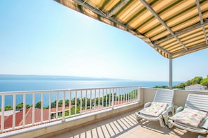 A balcony with two white lounge chairs, a metal railing, and a view of the sea and buildings in the background. - Apartments Dragana (Lokva Rogoznica)