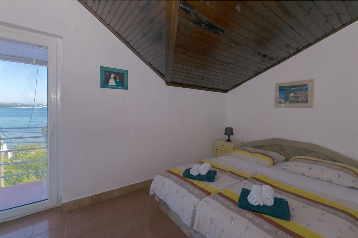 Un dormitorio con cama, mesita de noche y vista al mar a través de una ventana.