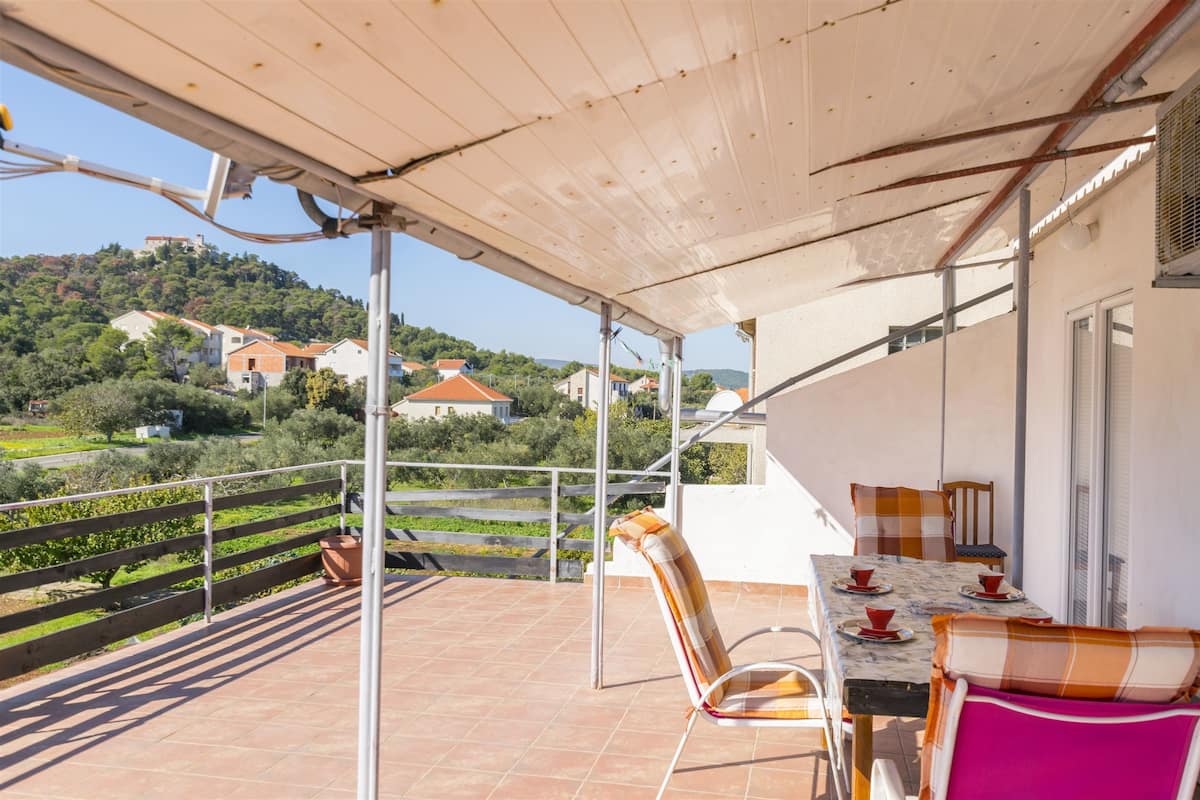 Un balcón con una mesa y sillas, con vistas a una colina con casas.