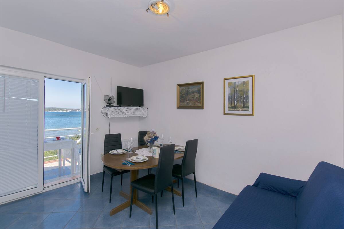 Comedor con una mesa dispuesta para cuatro, un sofá azul y vista al mar a través de un ventanal corredero.