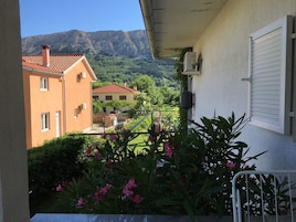 Un balcón con vista a la montaña, un edificio con techo rojo y un jardín con flores rosas.