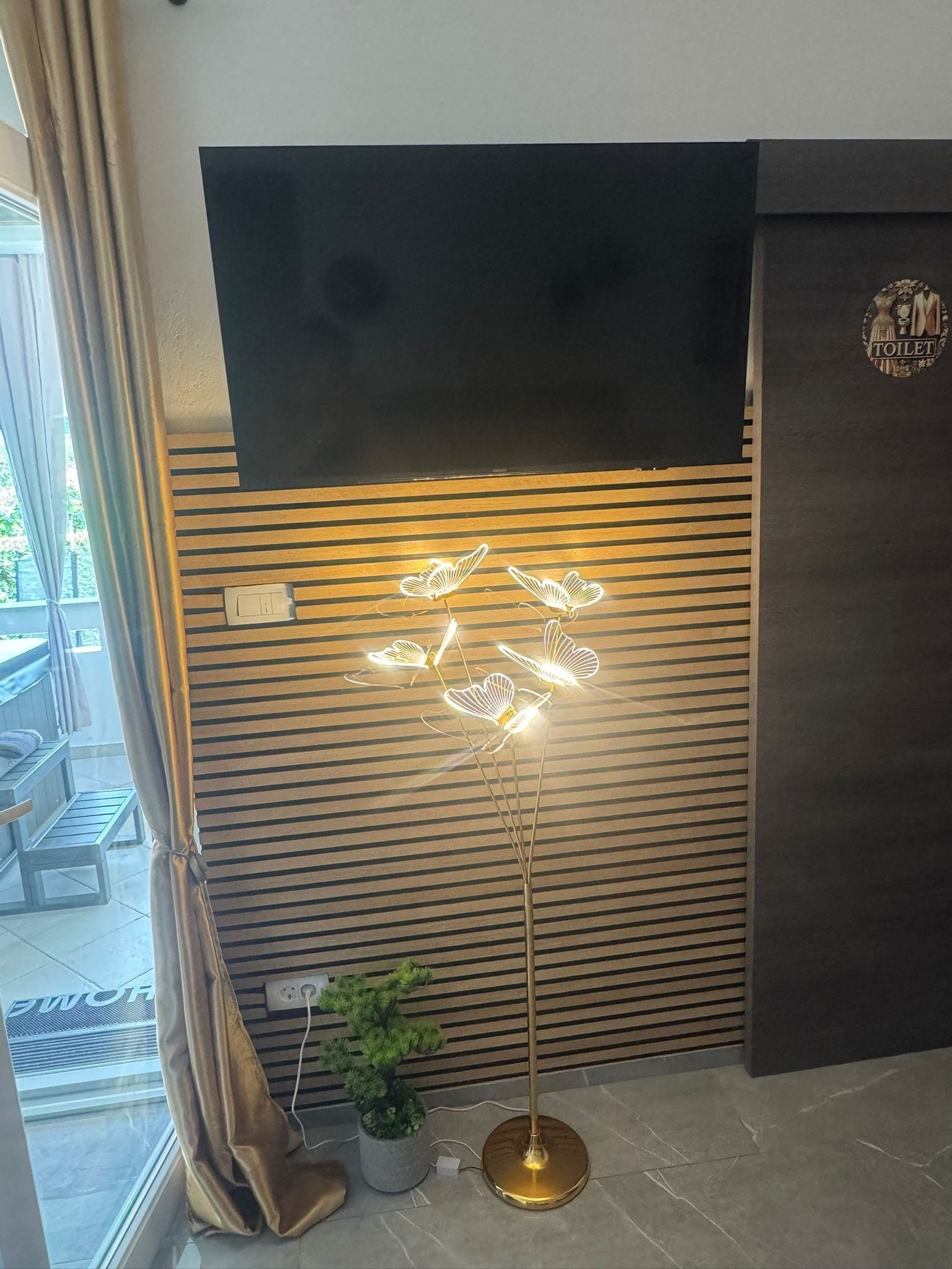 Ein modernes Zimmer mit Stehlampe, Topfpflanze und einem Schild, das eine Toilette kennzeichnet.