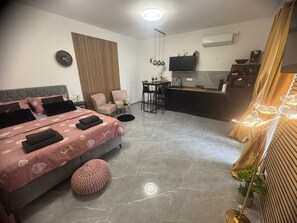 A modern hotel room with a bed, a desk, a chair, a small kitchen area, and a TV. - Apartments Bruno (Baska)