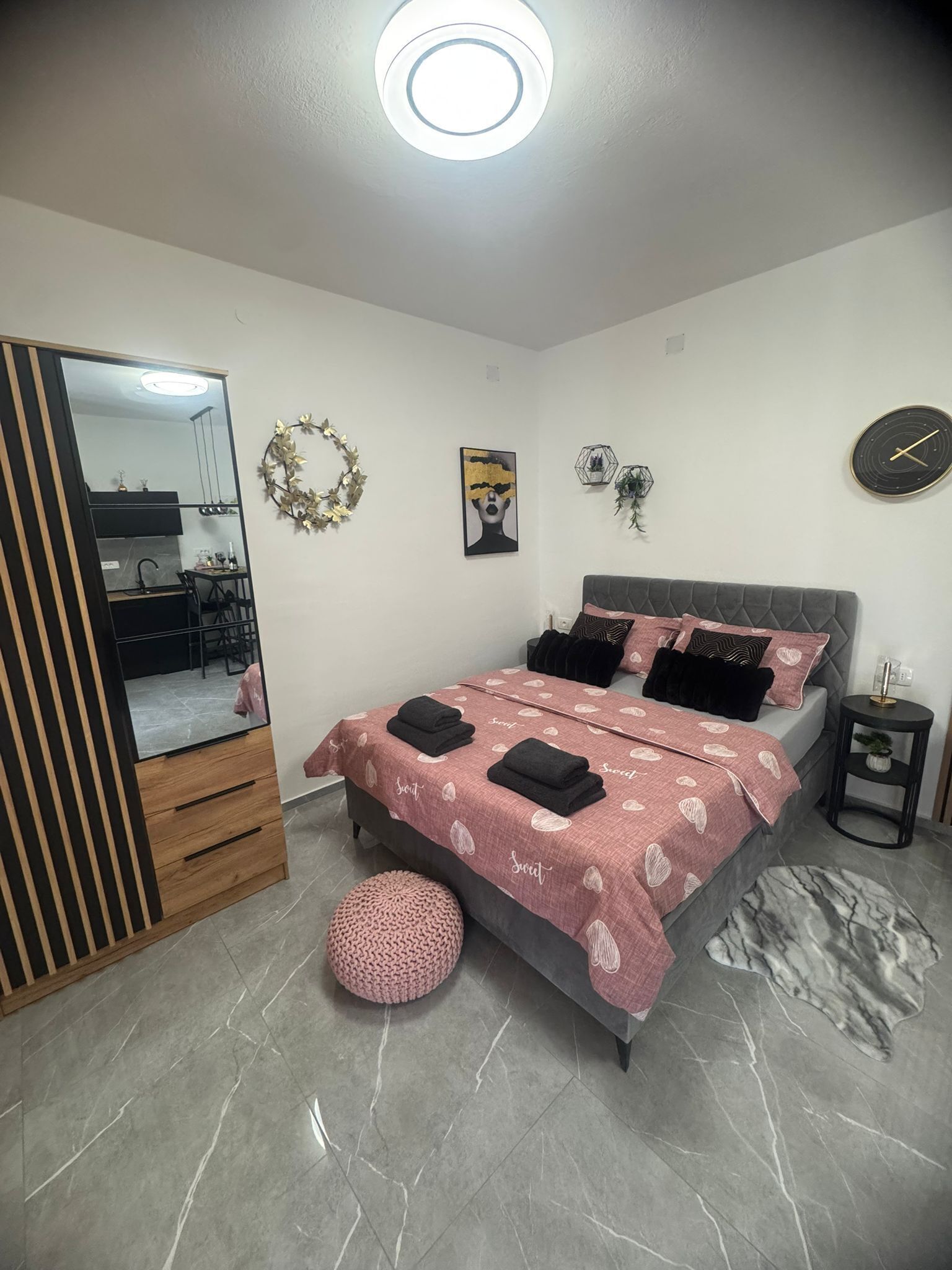 Une chambre à coucher avec un lit, un miroir, une horloge murale et une petite table ronde.