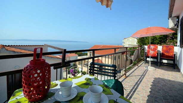 Un balcon avec une table dressée pour deux personnes, une lanterne rouge et une vue sur la mer.