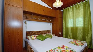 Une chambre à coucher avec une tête de lit en bois, un lit recouvert d’une literie à motifs floraux, une étagère au-dessus du lit et un rideau vert.