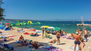 A beach with people sunbathing, swimming, and playing in the water. - Apartment Kralj (Selce)