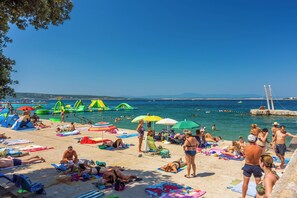 A beach with people sunbathing, swimming, and playing in the water. - Apartment Kralj (Selce)
