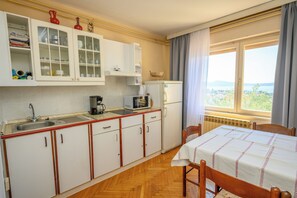 A compact kitchen with a sink, stove, and microwave, wooden cabinets, and a window with a view. - Apartment Kralj (Selce)