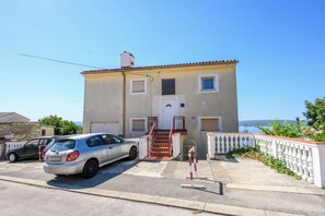 A two-story building with a white door and windows, a staircase with red railings, and a parked car in front. - Apartment Kralj (Selce)