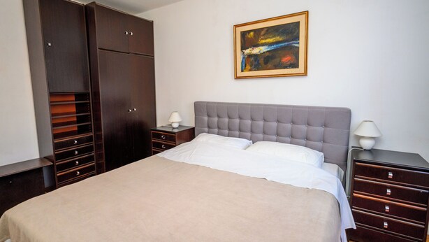 A bedroom with a large bed, a wardrobe, a nightstand, a lamp, and a painting on the wall. - Apartment Kralj (Selce)