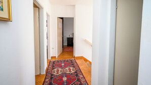 A hallway with a patterned rug, wooden flooring, and white walls. - Apartment Kralj (Selce)