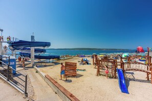 A beach with a water slide, sun loungers, and umbrellas. - Apartment Kralj (Selce)