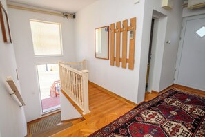 Eine Treppe mit hölzernem Geländer führt zu einer Zwischenebene, auf dem Boden liegt ein gemustertes Teppich und an der Wand hängt ein Spiegel.