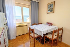 A room with a table set for two, a radiator, a window with a view of the sea, and a painting on the wall. - Apartment Kralj (Selce)
