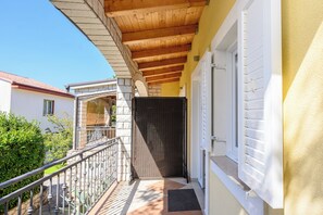 A covered outdoor area with a wooden ceiling, a metal railing, and a door leading to a building. - Apartment Kralj (Selce)