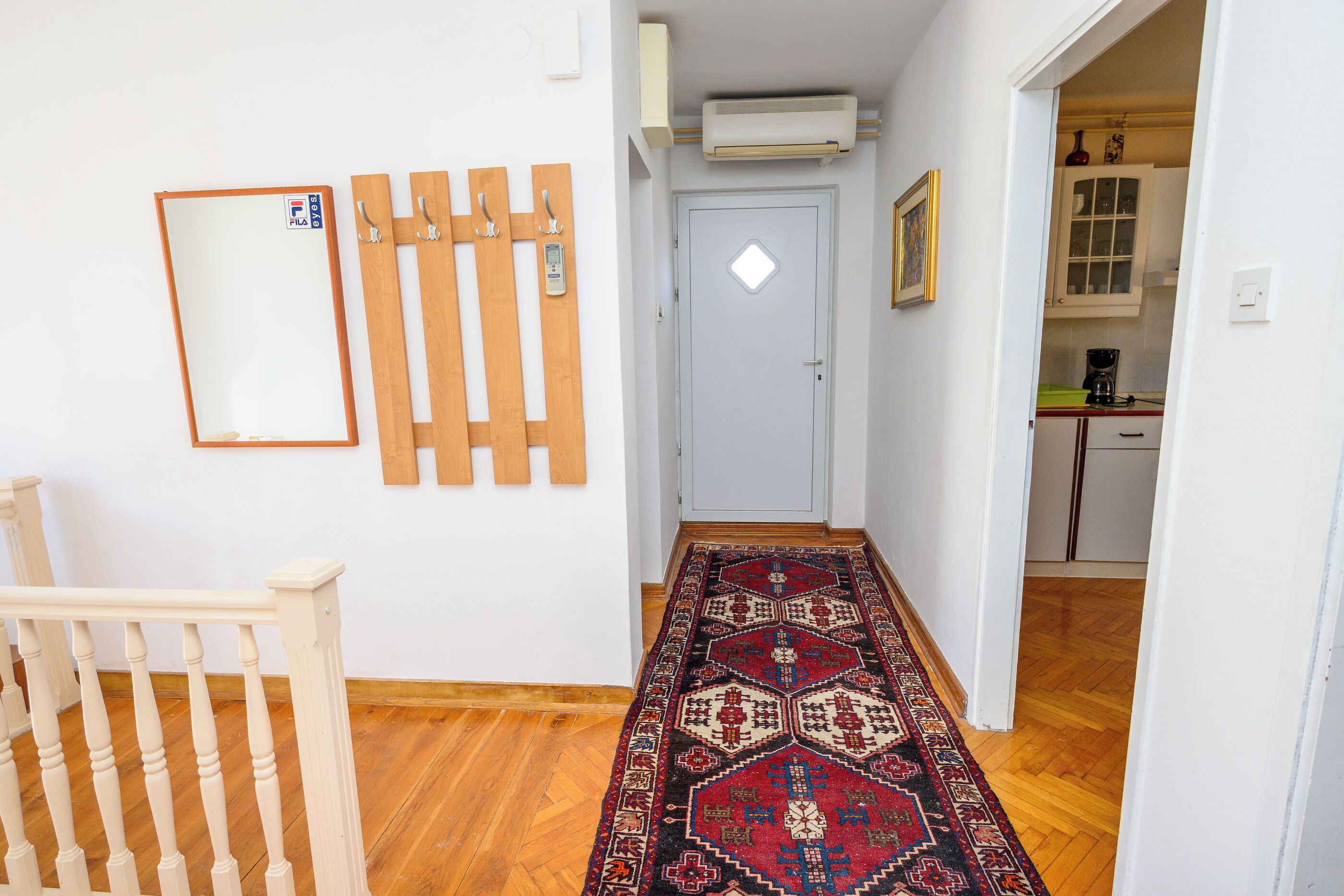 A hallway with a wooden floor, a patterned rug, a door with a handle, and a wall-mounted air conditioner.