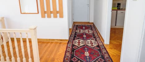 A hallway with a wooden floor, a patterned rug, a door with a handle, and a wall-mounted air conditioner.