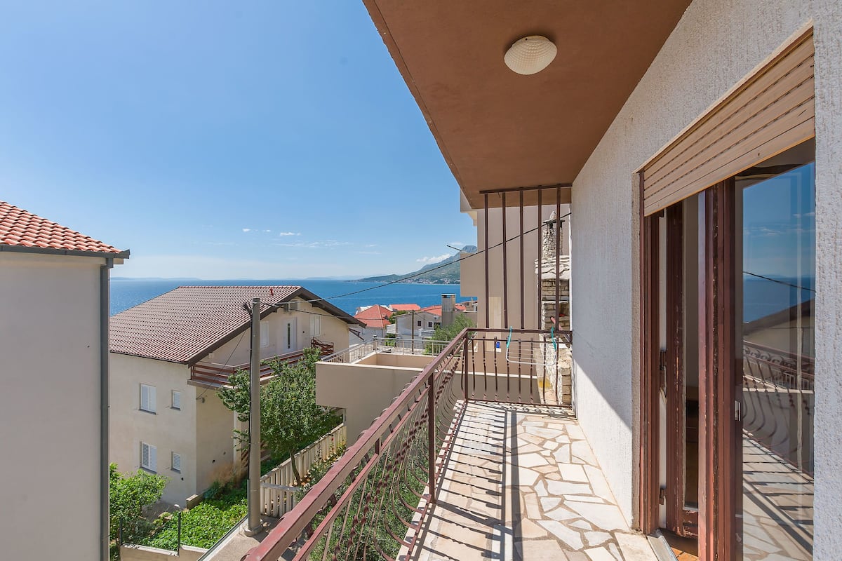 Ein Balkon mit Steinboden, Blick auf das Meer und umliegende Gebäude.