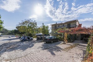 A paved driveway leading to a building with a balcony, parked cars, and a tree with autumn leaves. - Apartments Mario (Omis)