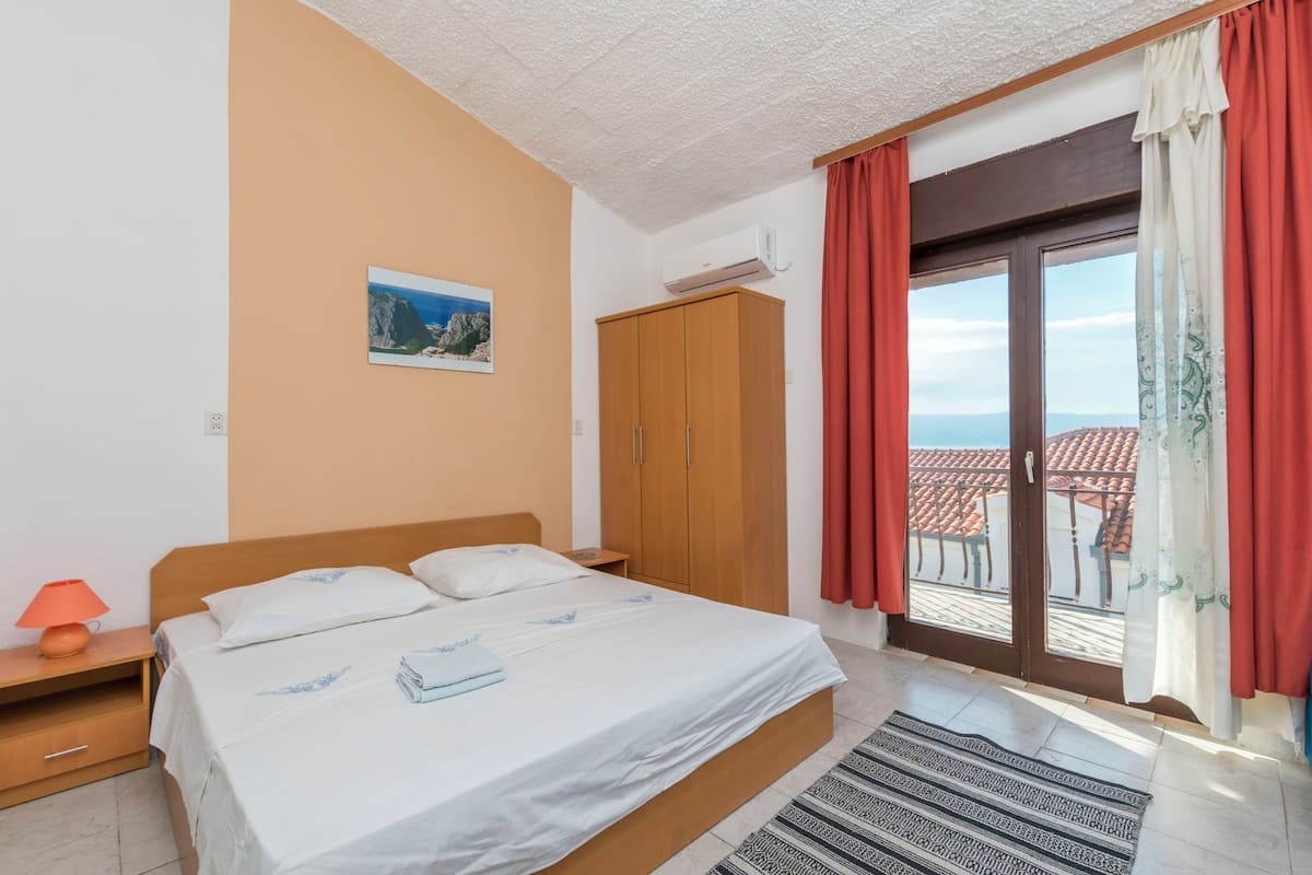 Ein Schlafzimmer mit Bett, Nachttisch, Schrank und Blick nach draußen.