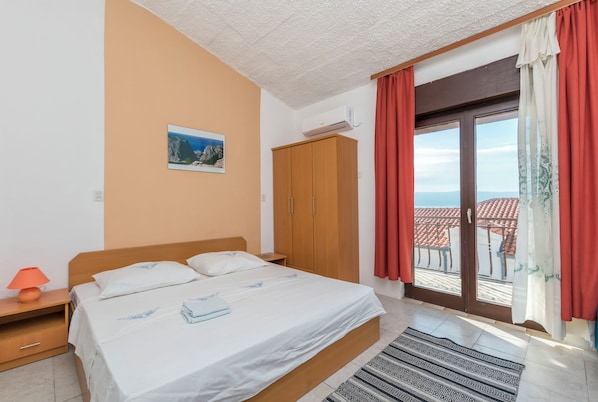 A bedroom with a bed, a nightstand, a wardrobe, and a view of the outside. - Apartments Mario (Omis)