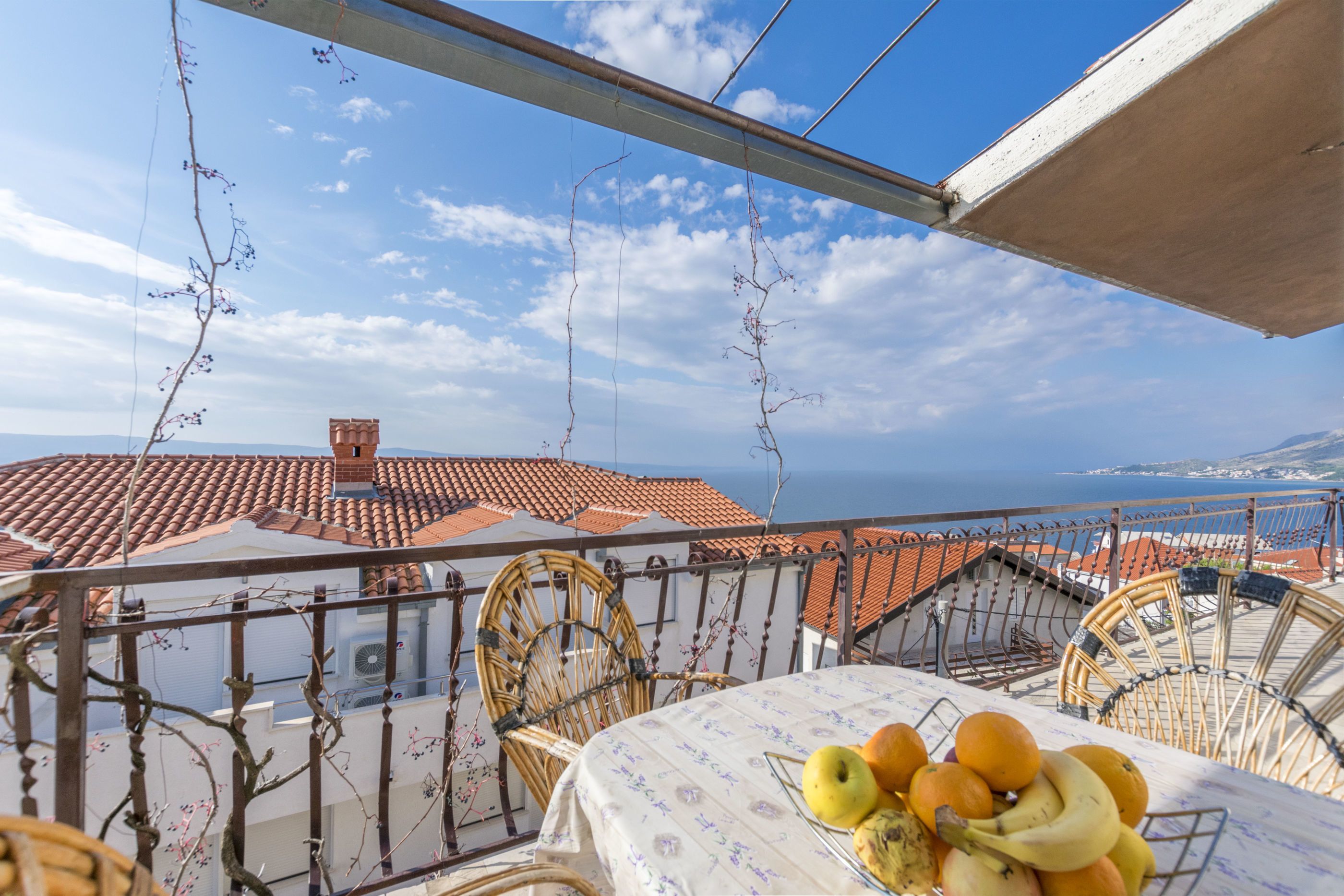 A balcony with a table set for breakfast, overlooking a coastal town with terracotta rooftops.