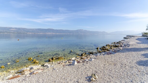 A pebbled beach with clear water and distant mountains. - Apartments Tomislav (Slatine)