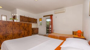 A bedroom with two beds, a wardrobe, a small kitchen area, and a window with curtains. - Apartments Tomislav (Slatine)