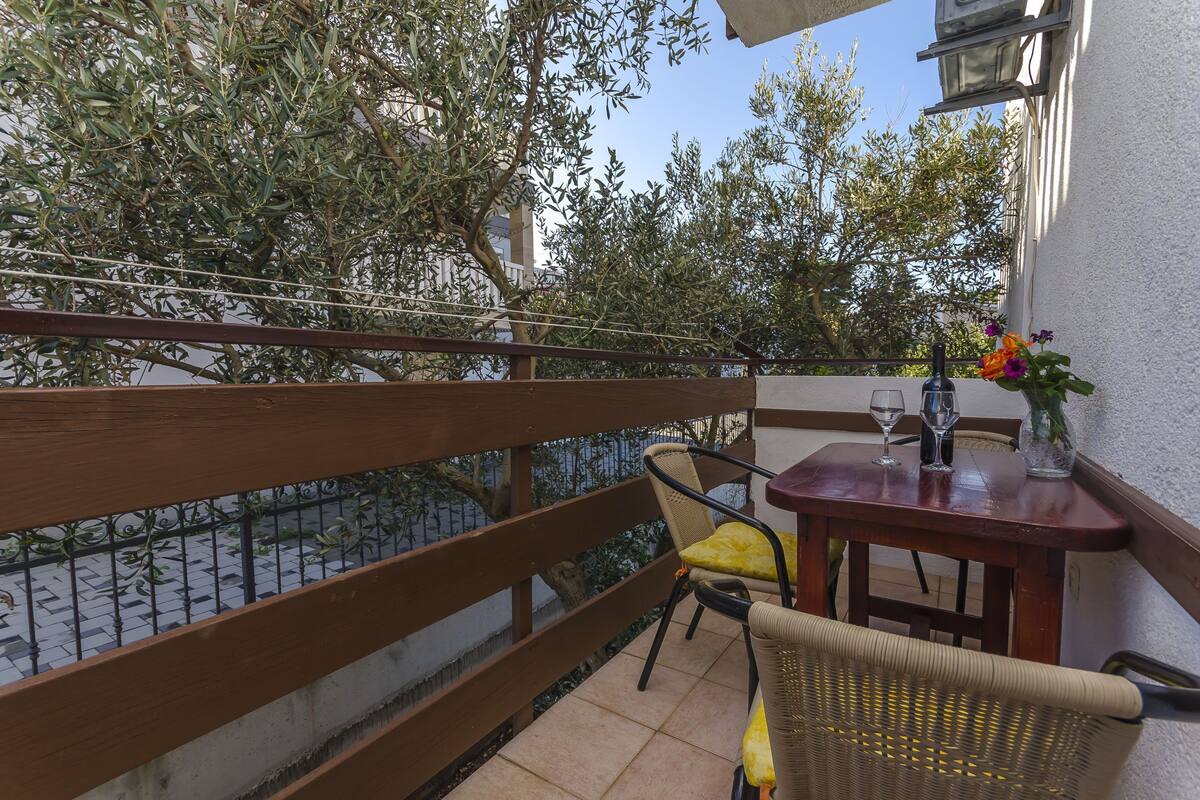 A balcony with a wooden railing, a wicker chair, a small table with a vase of flowers, and a bottle.
