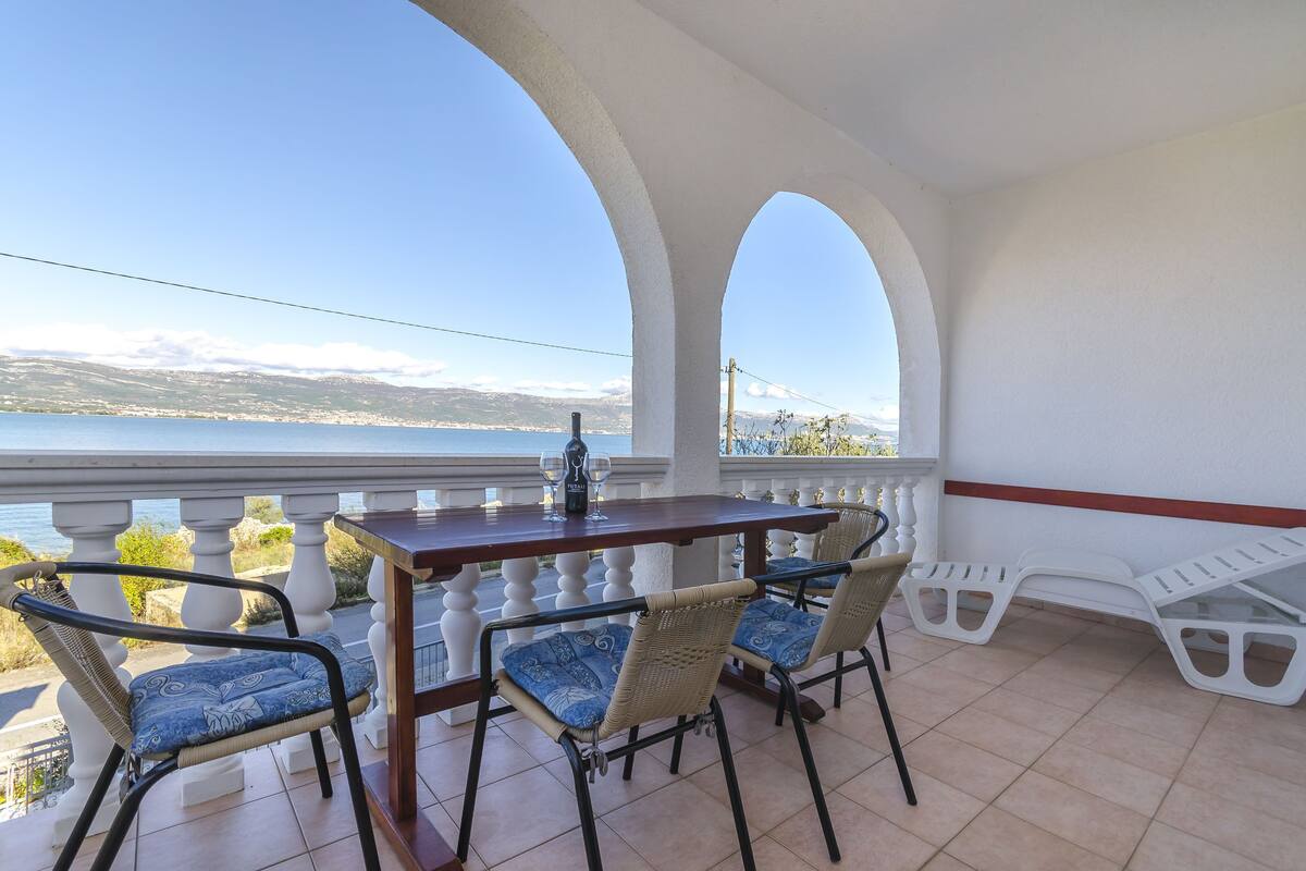 A balcony with a wooden table and chairs, overlooking a scenic view of a body of water and mountains.