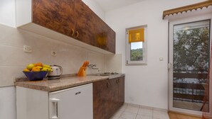 A kitchen with a countertop, a sink, and cabinets. There is a window with a view of trees and a balcony. - Apartments Tomislav (Slatine)