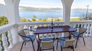 A terrace with a table and chairs, overlooking a body of water and a mountainous landscape. - Apartments Tomislav (Slatine)