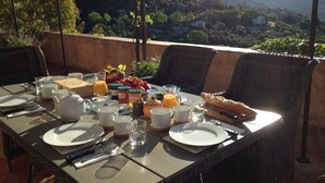 A breakfast table set outdoors with a scenic view of hills and a village in the background. - L'Estuve Provençale (Bargemon)