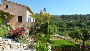 A stone building with a garden, a flag, and a view of a green landscape. - L'Estuve Provençale (Bargemon)