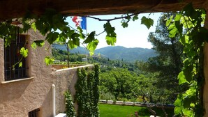 A view from a covered balcony with a vineyard in the background, a flag, and a stone building. - L'Estuve Provençale (Bargemon)