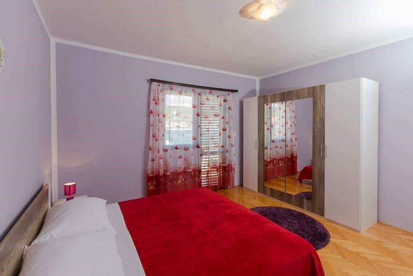 A bedroom with a bed, a wardrobe, a mirror, and a window with curtains.