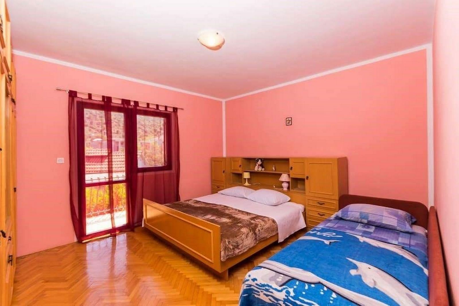 A bedroom with a wooden bed, a wooden wardrobe, and a window with red curtains.