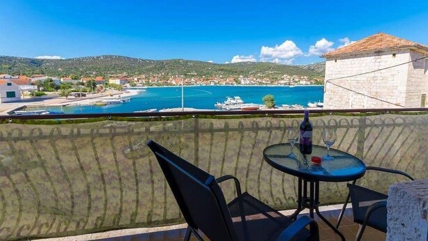 Ein Balkon mit Tisch und Stühlen mit Blick auf eine Küstenstadt, Boote und einen strahlend blauen Himmel.