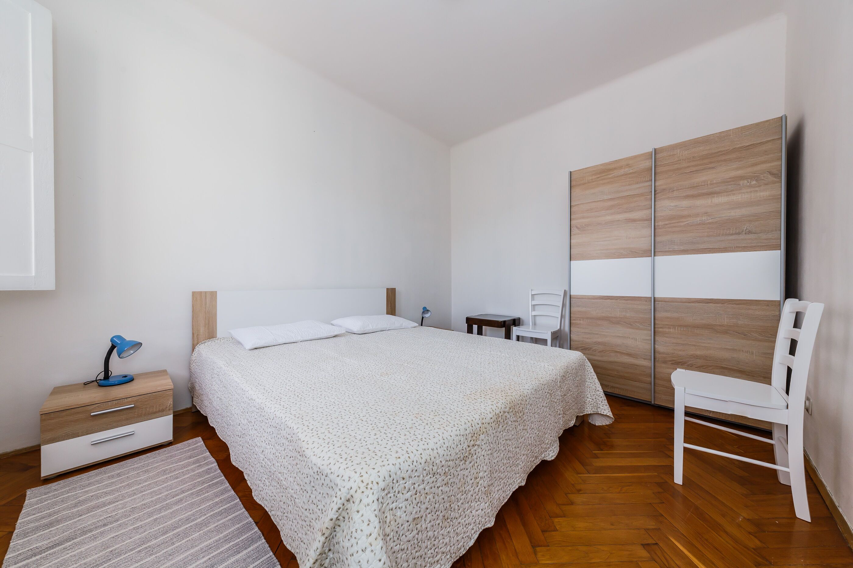 A bedroom with a bed, bedside table, chair, and wardrobe.