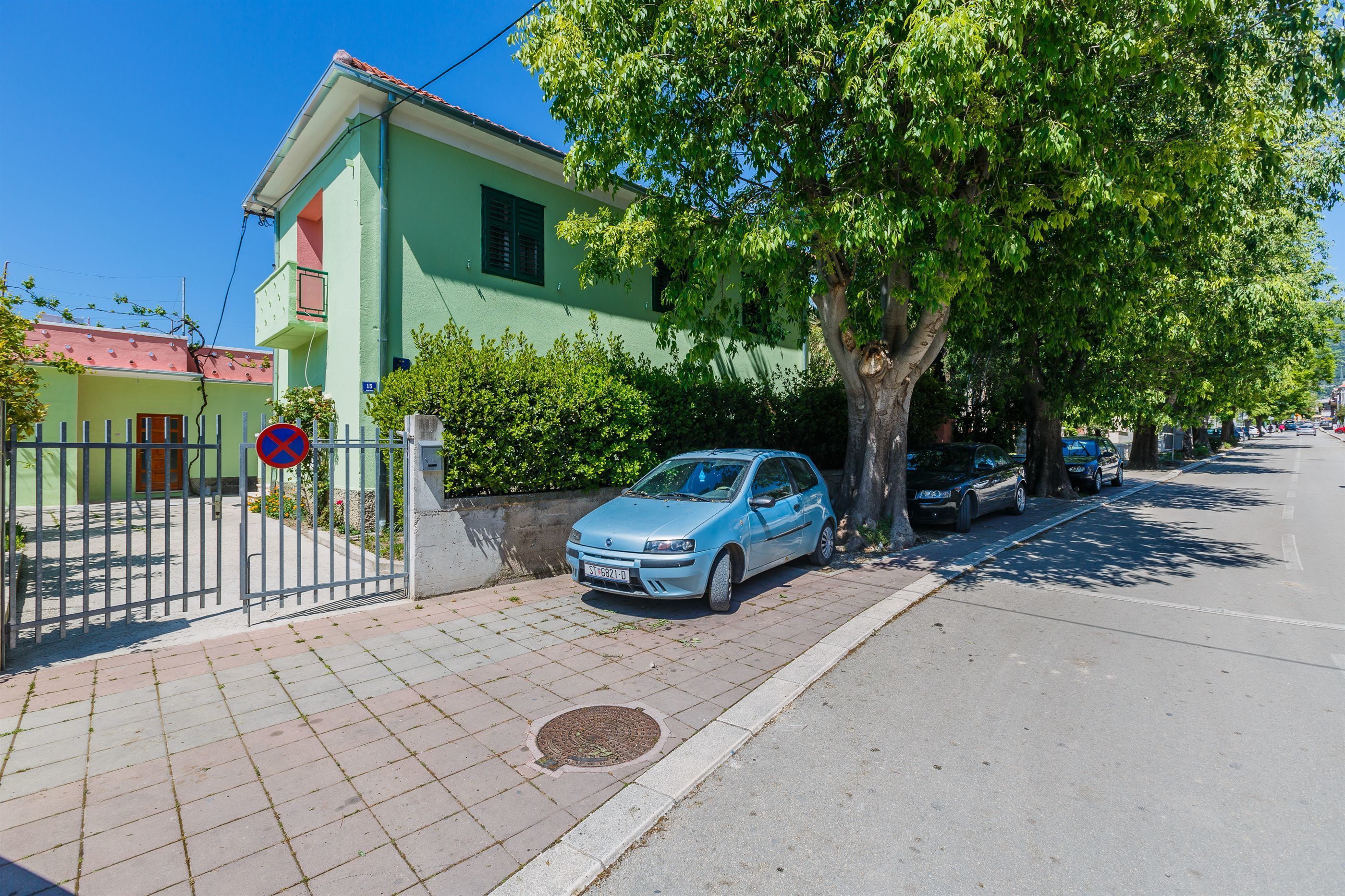 A residential street with a green house, parked cars, and a no parking sign.