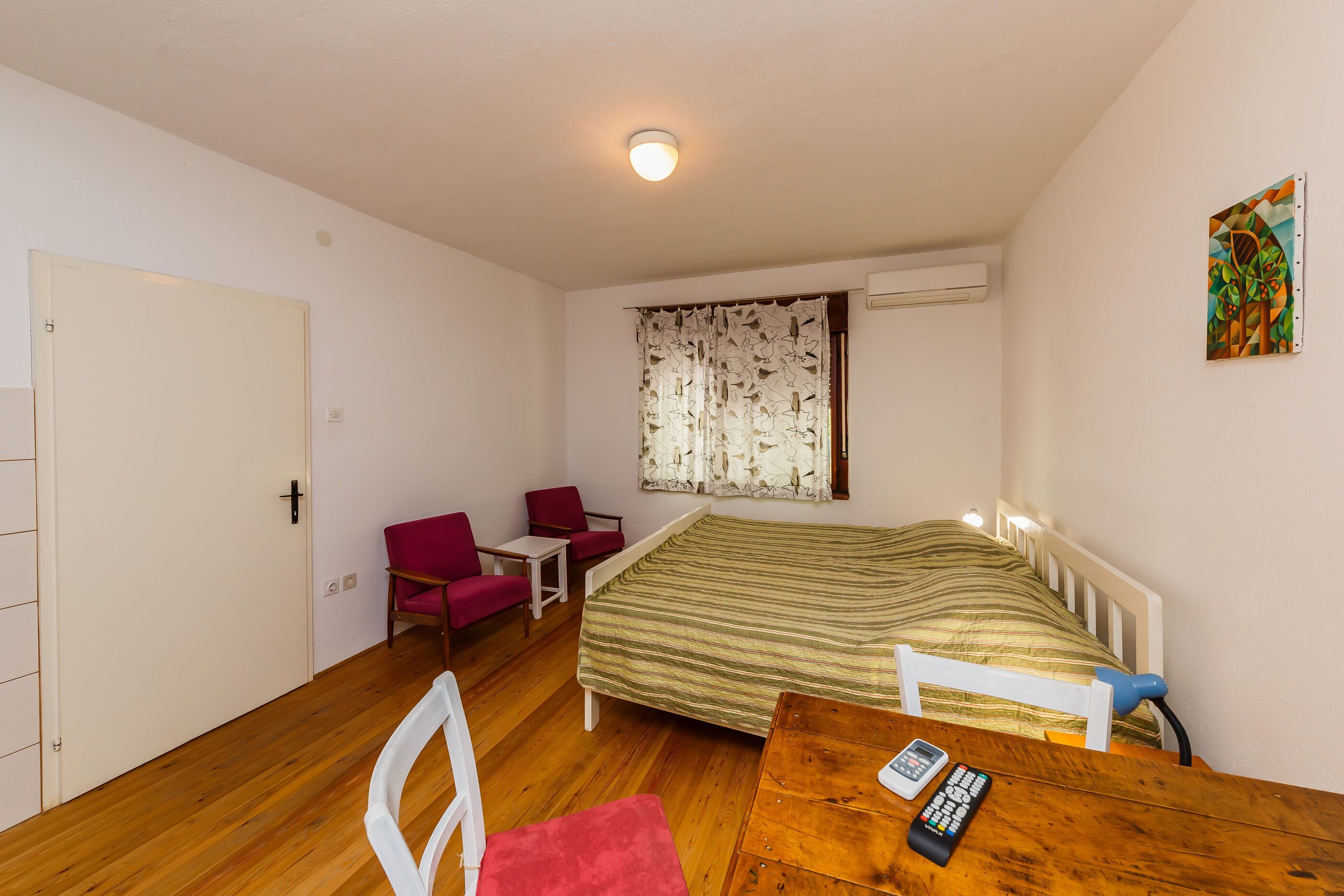A small, single-room accommodation with a bed, a desk, a chair, and a table.