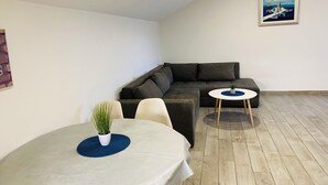 A modern living room with a sectional sofa, a round dining table with a plant, and a small side table. - Apartments Marija (Marina)