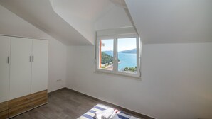 A bedroom with a large wardrobe, a window with a view of the sea, and a sloped ceiling. - Apartments Marija (Marina)