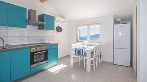 A kitchen with teal cabinets, a white dining table, and a white refrigerator. - Apartments Marija (Marina)