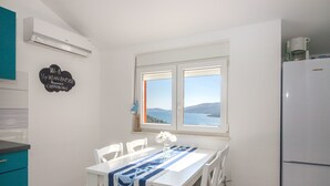 A kitchen with a white table, chairs, and a view of the sea through a window. - Apartments Marija (Marina)
