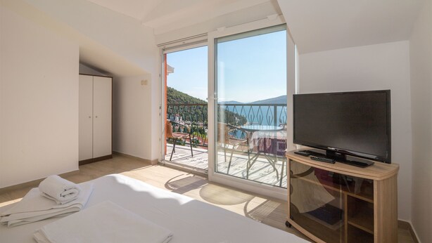 A hotel room with a balcony, a television on a wooden stand, and neatly folded towels on the floor. - Apartments Marija (Marina)