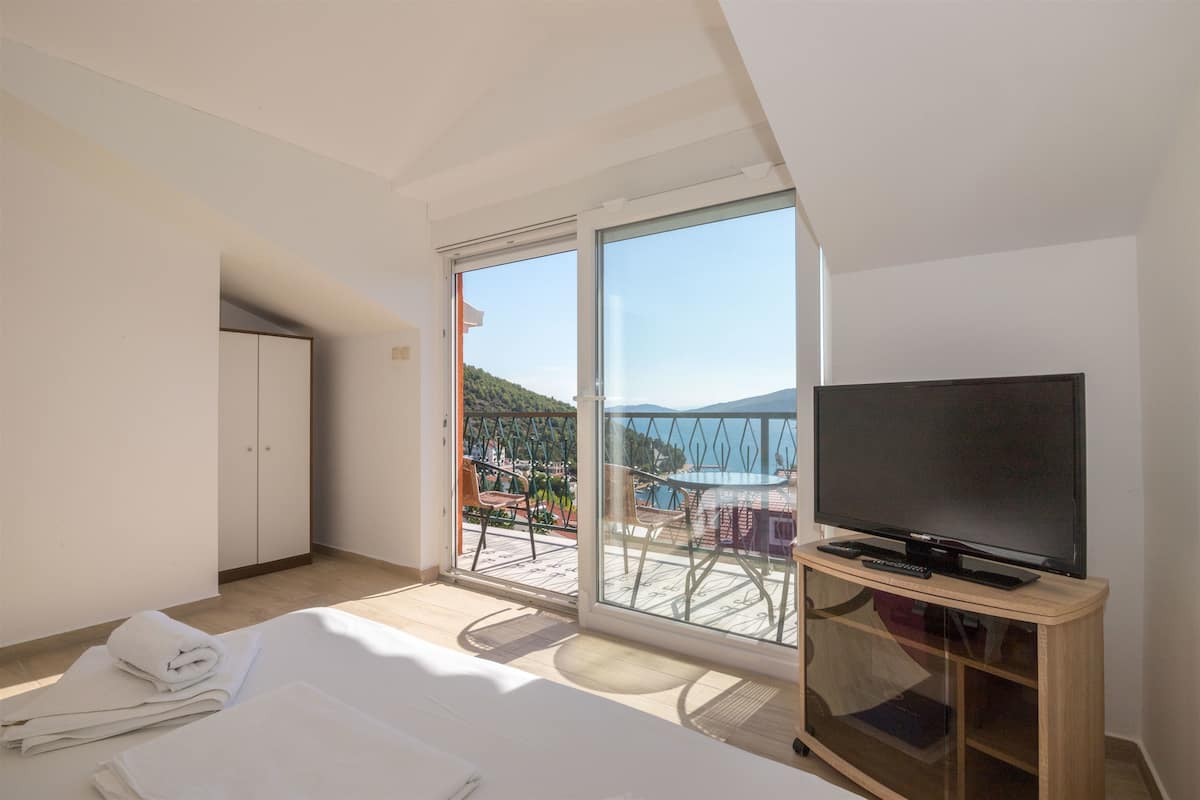 A hotel room with a balcony, a television on a wooden stand, and neatly folded towels on the floor.