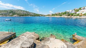 A coastal scene with clear turquoise water, rocky shore, and buildings on a hillside. - Apartment Vukorepa (Razanj)